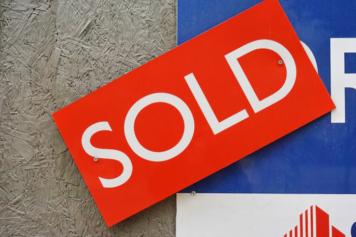 Red sold sign nailed to an estate agent’s ad