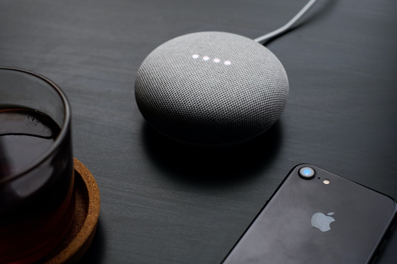 A Google Nest Mini speaker sits between a glass of black coffee and an iPhone