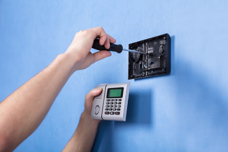a man installing a security system on a blue wall