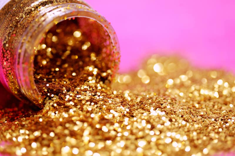 A pot of gold glitter spills over against a pink backdrop