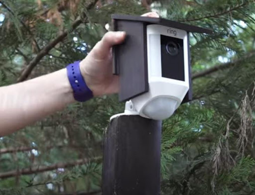 a hand puts the black wooden camera cover over a ring outdoor camera
