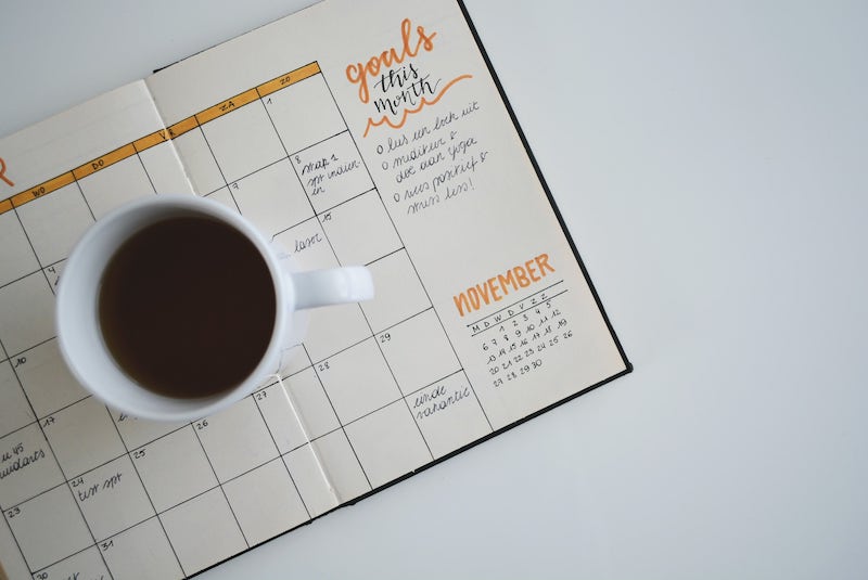 A cup of coffee sits on a diary with a schedule and a list of goals for the month.