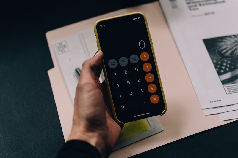 A phone calculator is held above some financial documents.