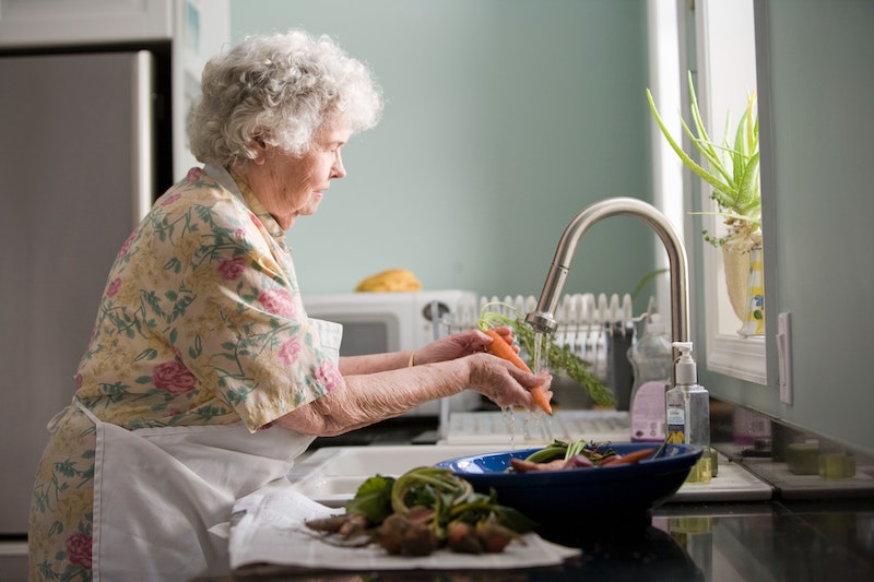 An elderly lady prepares food at the sink.