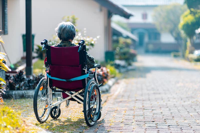 An elderly woman sits in a wheelchair on a brick road