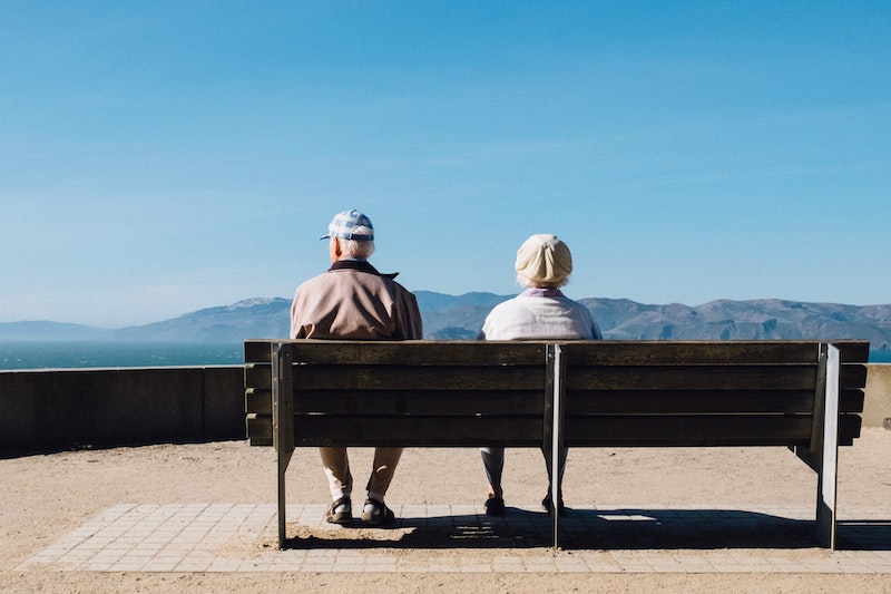 An old couple sit on a bench in front of a mountain view