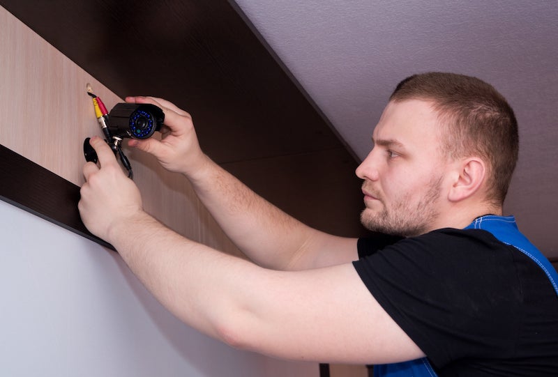 a man installing a black security camera on a wall