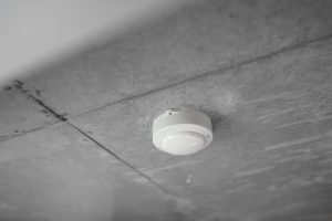 a white fire alarm installed on a gray ceiling.