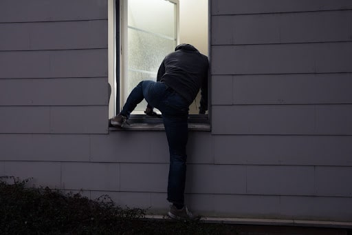 A man trying to break in to a house through an open window.