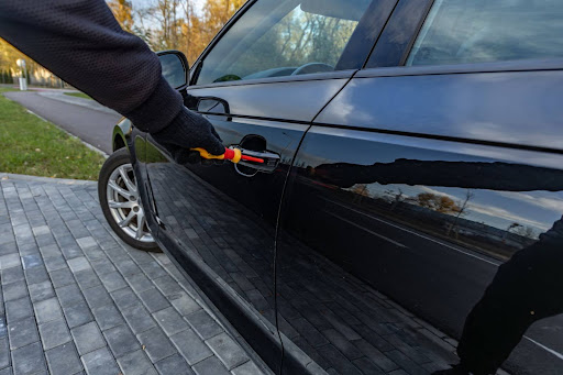 A burglar tampering with a keyless entry system on a car.